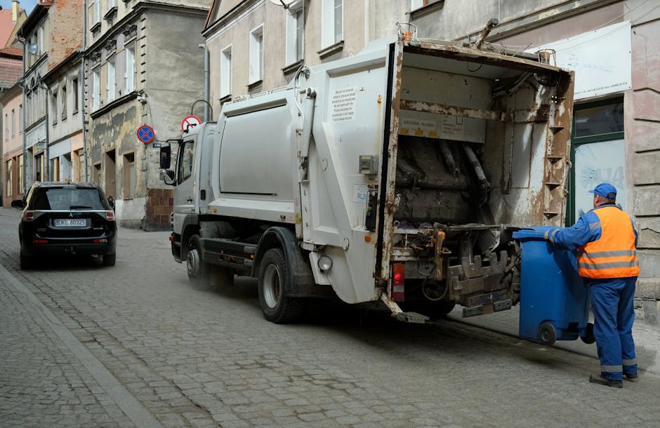 Two large black garbage bags filled with waste materials are positioned on the pavement near the curbside in an outdoor urban setting. The bags are made of thick plastic and appear tightly packed, wit