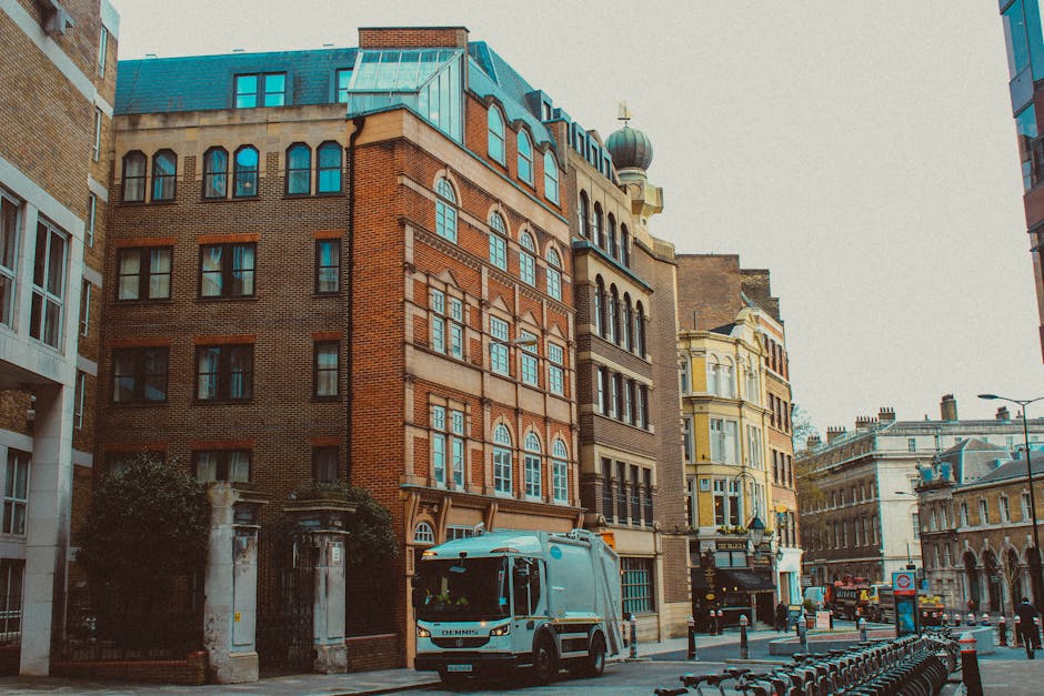 The image shows a city street scene featuring a modern red double-decker bus with a sleek design and large front windows, positioned centrally on the road. The bus displays the route number 8 on an el